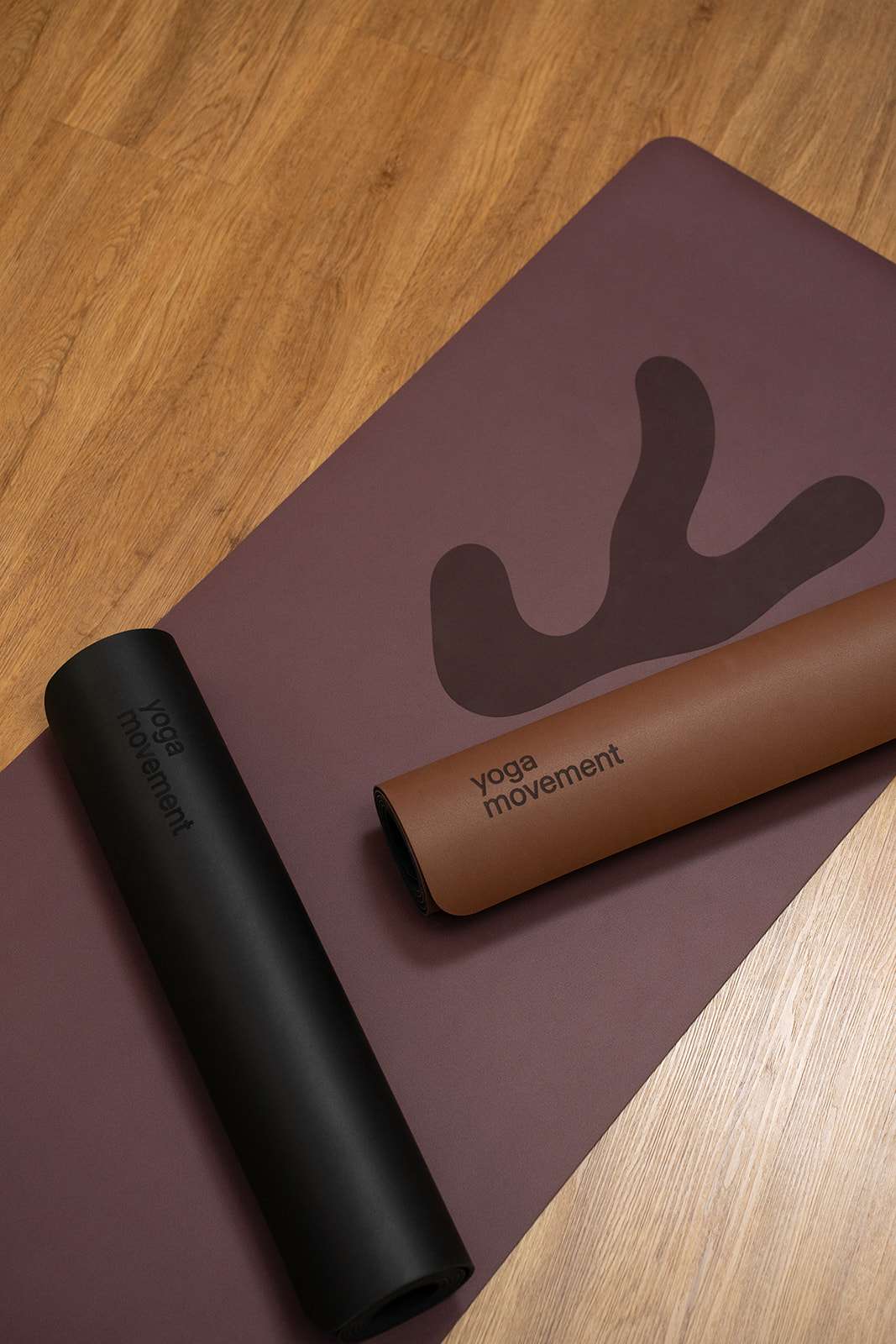 Detailní pohled na strukturu vínové jogamatky s elegantním logem Yoga Movement na dřevěném pozadí.
